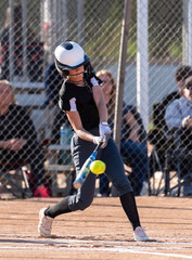 Female high school softball player flinging the bat aside as she postures to spint up the first base line.
