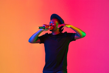 Young african-american musician singing on gradient orange-purple studio background in neon light....