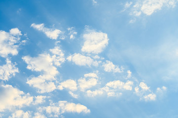 White clouds on blue sky with sun rays from below, for background