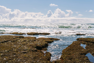 Tide pools with crashing ocean waves on sunny day with clouds in sky