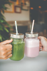 Woman hand holding healthy smoothie in eco friendly glass jar with paper straws in a luxury gym recreation area or vegan cafe. Trendy muted toning, place for text