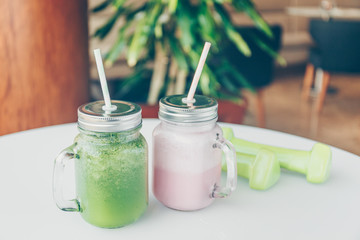 Healthy smoothie options in eco friendly glass jars with paper straws and light dumbbels in a luxury gym recreation area or vegan cafe. Trendy muted toning, place for text