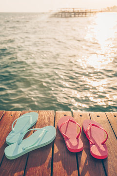 Two pairs of flip flops at the wooden pier during sunset. Luxury vacation resort. Holiday getaway concept. Vertical, warm toning