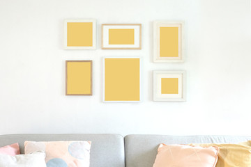 multi poster in wooden frames on a white wall, minimal interior with grey sofa and colourful pillows, blank space to put pictures