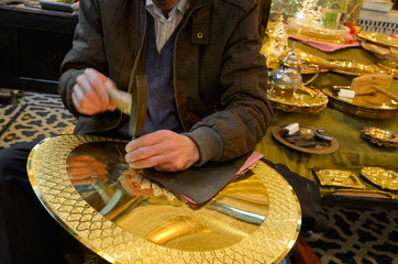 Worker with hammer and chisel engraving complex patterns on brass plate in Fes Morocco