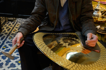 Worker with hammer and chisel showing work in progress engraving brass plate in Fes Morocco