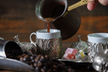 Fototapeta na wymiar Pouring turkish coffee into vintage cup on wooden background with turkish delight