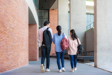 Asian three students are walking and talking together in university hall during break in...