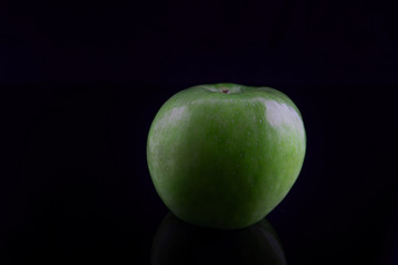 Green apple with reflection, on a black background, shallow depth of field. Concept, healthy food, lifestyle.