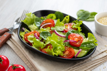 Healthy vegetable salad from fresh vegetables of tomato, spinach, cucumber, lettuce and sesame on a plate. Useful nutrition.