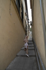 stylish moslem woman wearing white coat and beige scarf walking on the stair between the wall of the buildings