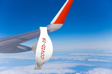 A protective medical mask hangs on the wing of an airplane. The concept of the spread of viral diseases. The inscription COVID-19