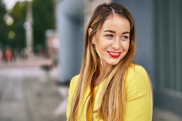Obraz premium Portrait of a young beautiful laughing woman with long hair and a yellow jacket against the background on a cloudy day. Close-up.