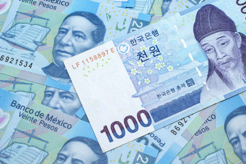 Fototapeta premium A blue South Korean one thousand won bank note close up in macro on a background of Mexican twenty peso bank notes