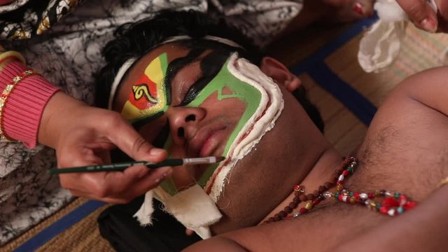 Make up artist polishing the chutty paste on the face of a Kathakali dancer. 