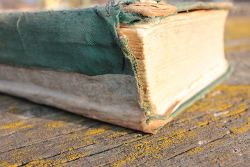 Old shabby book on a rough wooden table covered with moss outdoors. 
