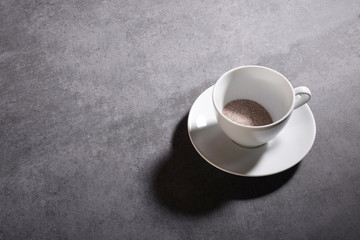 High angle view instant coffee granules in a porcelain coffee cup on the gray stone texture with...