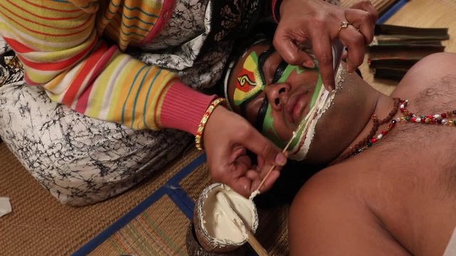 Make up artist pasting Chutty on the face of a Kathakali dancer. 