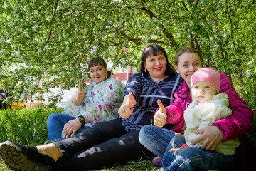Fototapeta premium Three different funny women and one small seriously girl in the park full of apple blossom trees in a spring day. Aunts and niece in nature landscape