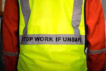 Close-up at "Stop work if unsafe" sign label on back of reflective vest which is wear by a lifting signaler worker. Safety conception photo for heavy industry operation.