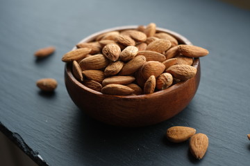 Almonds nut close-up.Raw almonds in a round  cup on a black slate background. Nuts in a cup.Vegetarian and vegan food.Healthy food.