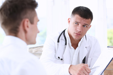 Concerned handsome doctor communicate with patient holding silver pen and showing pad. Physical agreement signature, disease prevention, consent sign, 911, prescribe remedy, healthy lifestyle concept