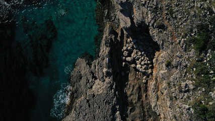 Aerial top down view of beautiful young woman in long white dress lying on rocky coast with cracks in rocky surface. Azure Adriatic sea, foaming waves. Kotor bay, Lustica peninsula, Montenegro. 