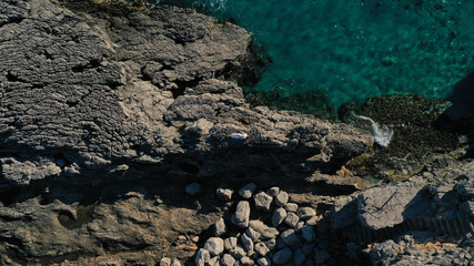 Aerial top down view of beautiful young woman in long white dress lying on rocky coast with cracks in rocky surface. Azure Adriatic sea, foaming waves. Kotor bay, Lustica peninsula, Montenegro. 