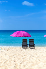 Pink beach umbrella and chairs on beautiful beach with clear blue sky, summer outdoor day light, relaxing on summer break, holiday season
