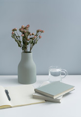 There are pink roses in the vase on the white desk, as well as books and notebooks