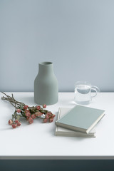 There are pink roses in the vase on the white desk, as well as books and notebooks