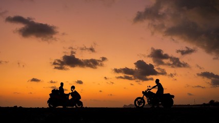People on motorcycles in silhouettes at sunset time near sea coast line