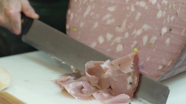 Butcher slicing organic Italian Bologna sausage mortadella, a traditional pork sausage, with a sharp knife to prepare a delicious ban. Buns with mortadella, food.