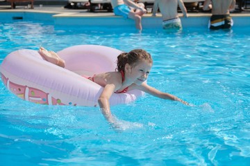 Summer vacation, child resting on swimming ring in outdoor pool