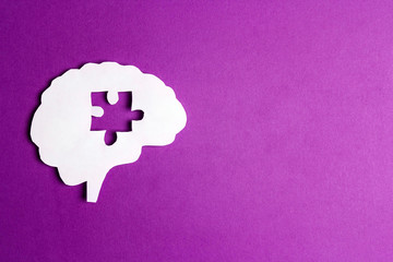 Brain paper symbol with a puzzle piece cut out on the purple background. Mental health symbol.