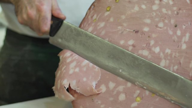 Butcher slicing organic Italian Bologna sausage mortadella, a traditional pork sausage, with a sharp knife to prepare a delicious ban. Buns with mortadella, food. Slow motion.