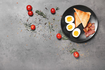 Plate with boiled eggs, bacon and toasted bread on dark background