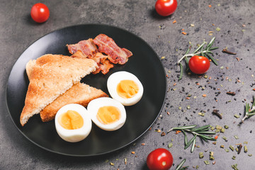 Plate with boiled eggs, bacon and toasted bread on dark background