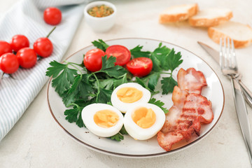 Plate with boiled eggs, bacon and tomatoes on white background