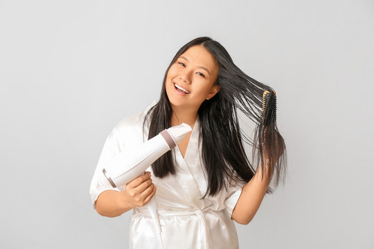 Beautiful Asian woman with hair dryer on light background