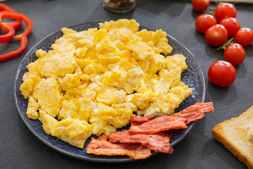 Plate with scrambled egg and bacon on dark background
