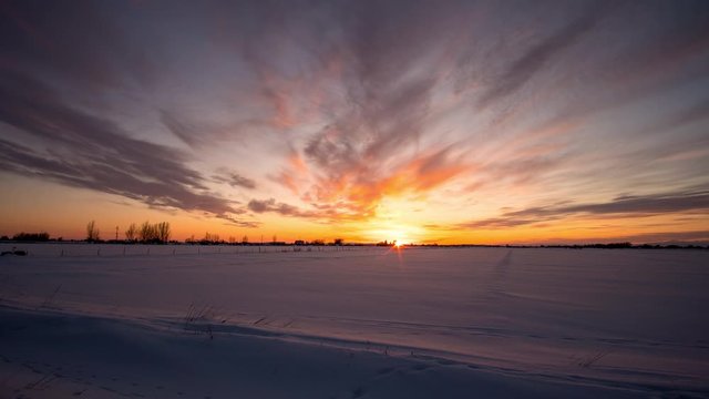Sunset time lapse over winter landscape in Idaho with vibrant clouds as the sun disappears in the distant horizon.
