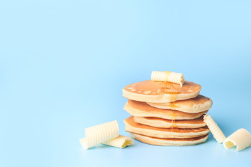 Tasty pancakes with honey and butter on color background