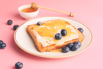 Tasty toasted bread with honey, butter and berries on color background