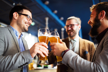 Happy young businessmen drinking beer and talking at pub after work