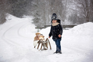 Fototapeta na wymiar Cute boy playing with teddy bear in the snow, winter time. Little toddler playing with toys on a snowy day