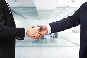 Two businessmen shake hands on the background of sunny modern furnished office, deal concept, close...