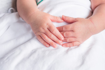 Hands of newborn baby on white cloth with copy space. Close-up of baby hands. Selective focus. Love of family concept