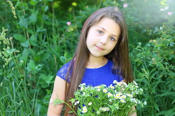 beautiful girl in a blue dress with a bouquet of daisies and a wreath of wildflowers in the summer botanical garden
