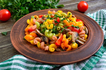 Tasty warm salad. Colored pasta with mushrooms and fresh tomatoes in a bowl on a wooden table. Pasta colorata.